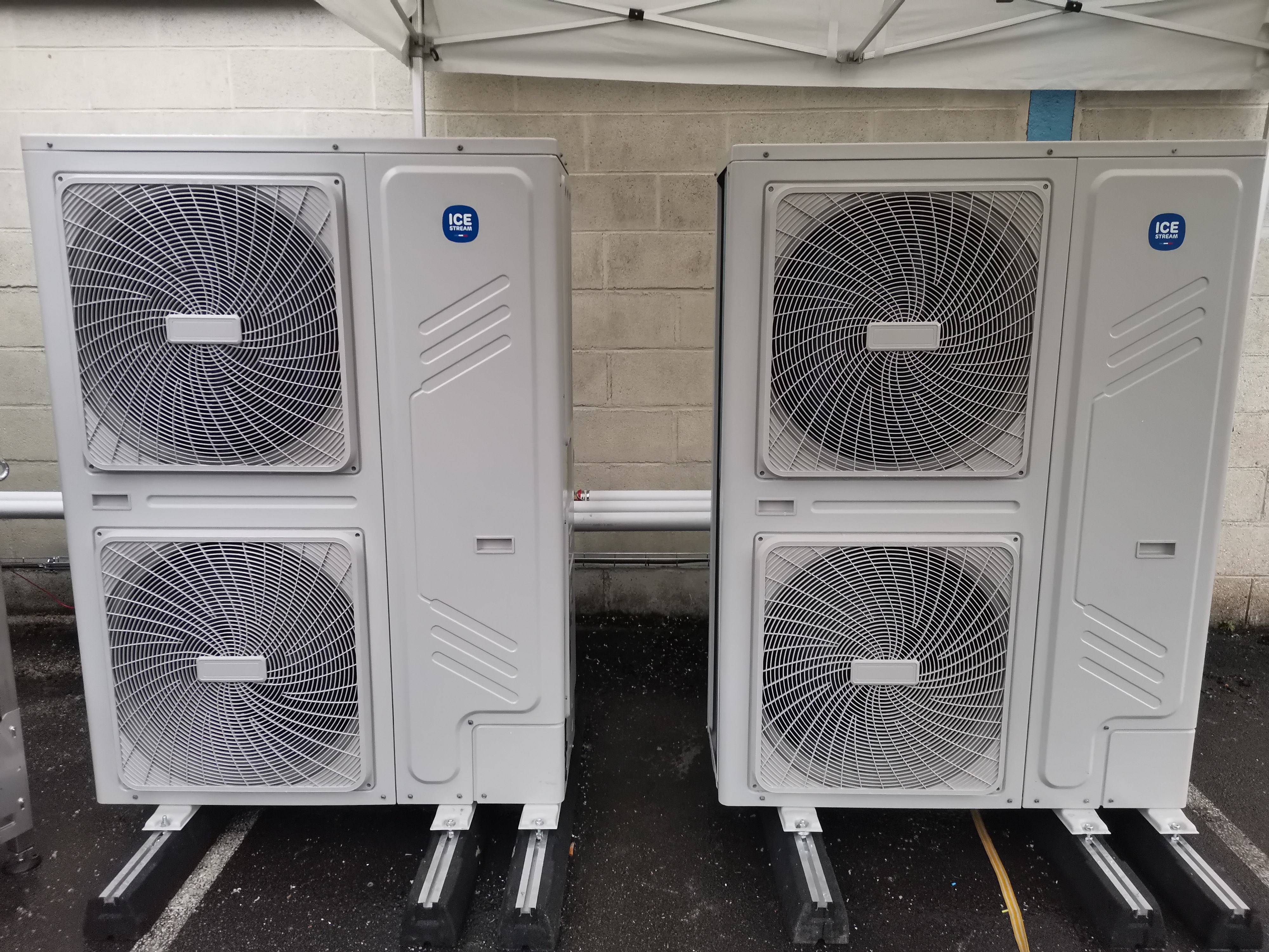 icestream-pac-1 Deux pompes à chaleur Air-Eau de la marque Ecofeel installées à l’extérieur d’une usine, montées sur des supports métalliques, avec un mur en arrière-plan.